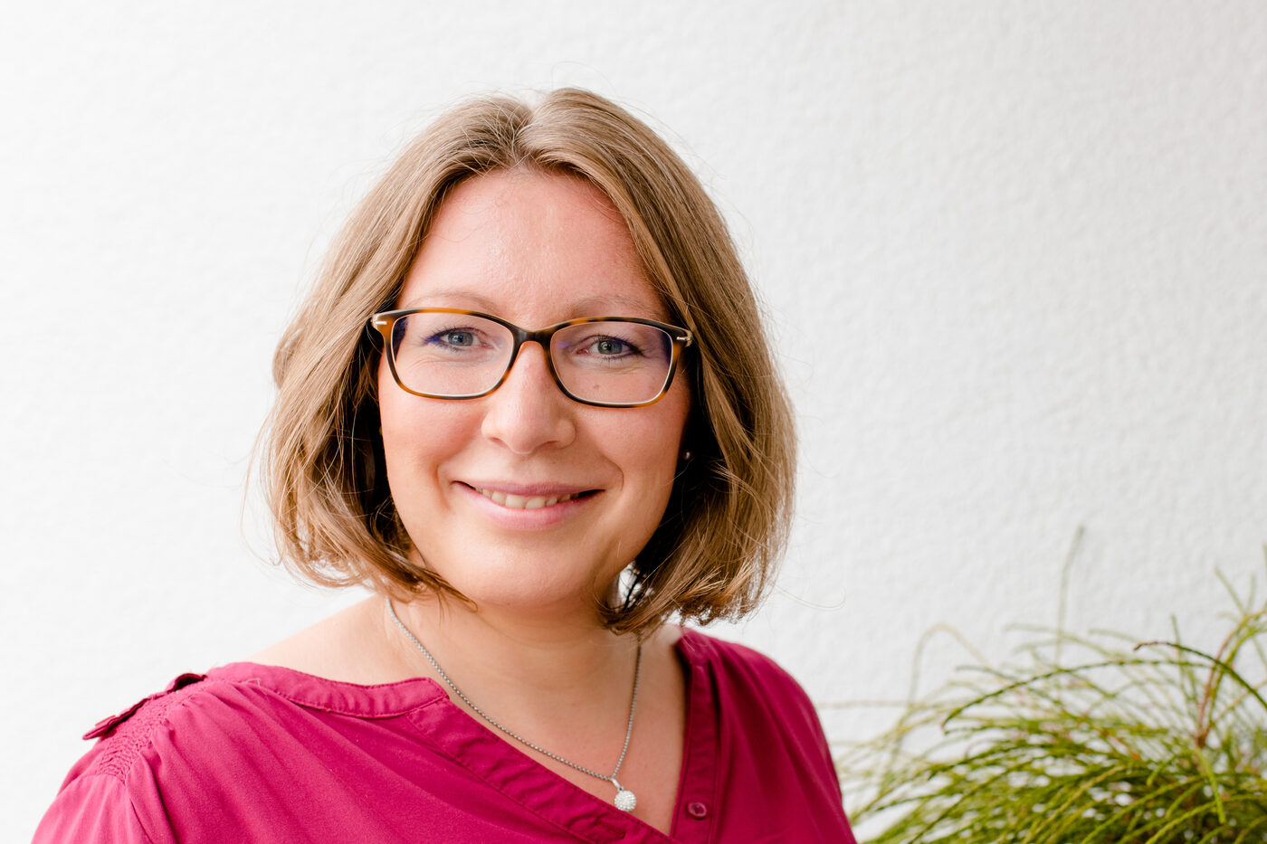 Kerstin Hiemer lächelt freundlich in die Kamera, neben einer Grünpflanze
